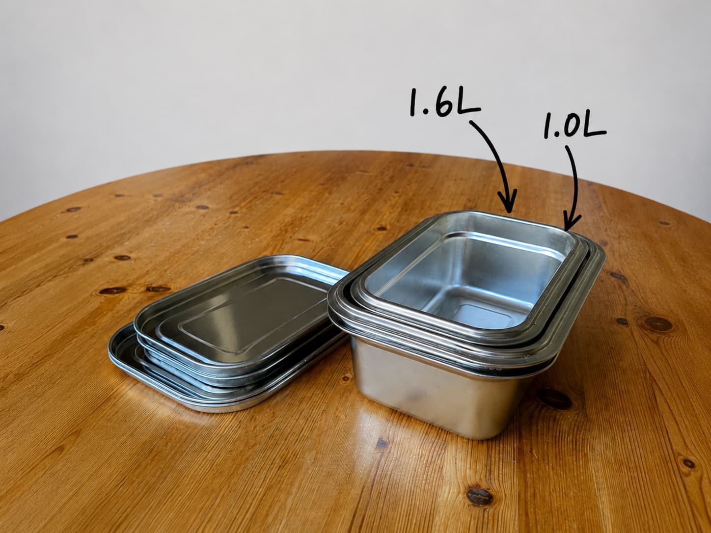 The full Loopware set nested to a single footprint — 1.0L containers inside the labelled 1.6L, with all four steel lids stacked flat beside.