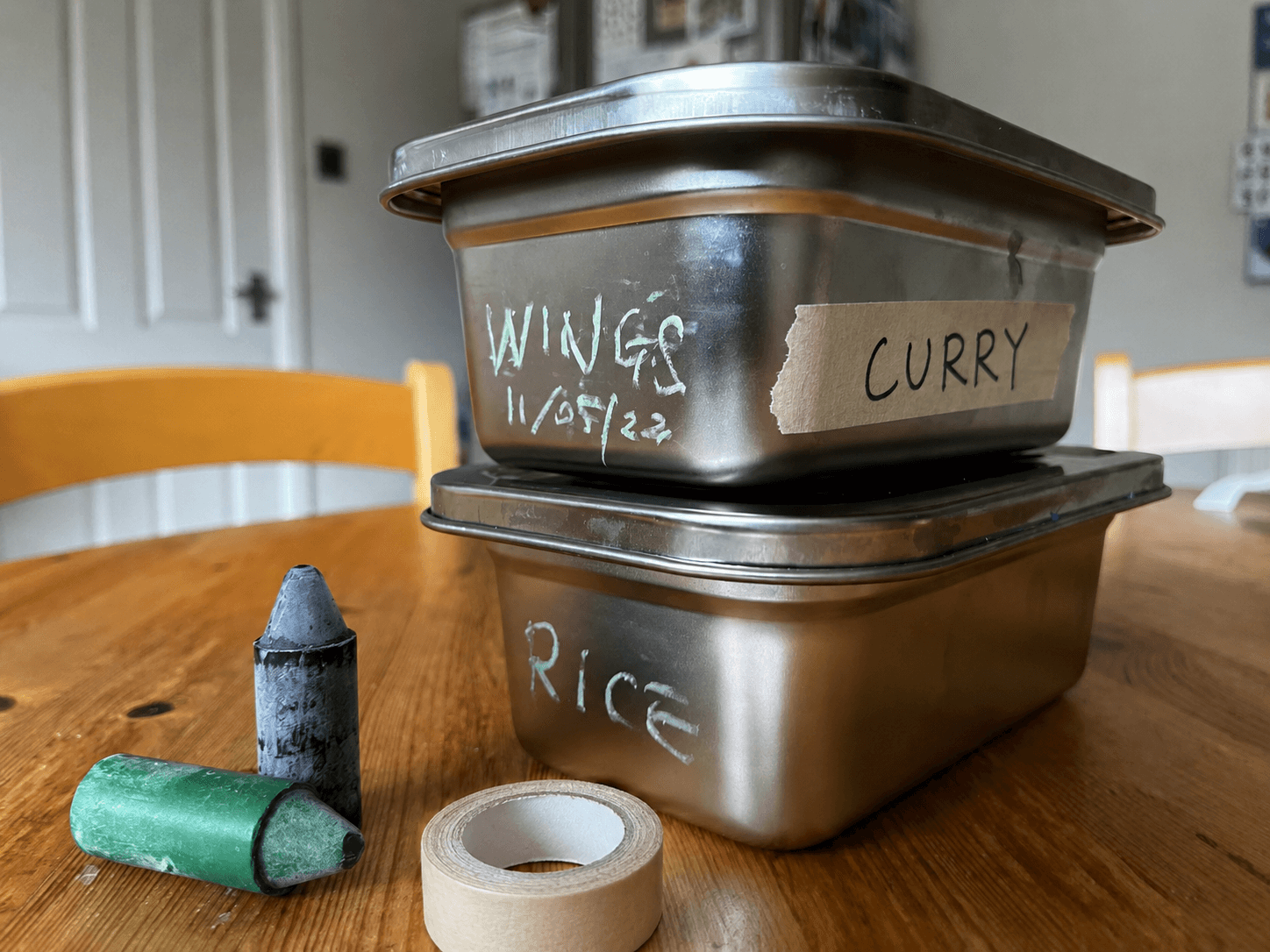 Two Loopware stainless steel containers labelled by hand — chalk-pen marking and a strip of tape reading CURRY and RICE.